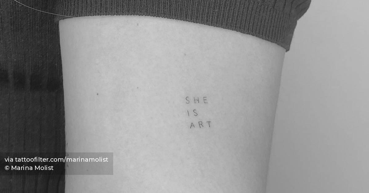 "SHE IS ART" lettering tattoo on the upper arm