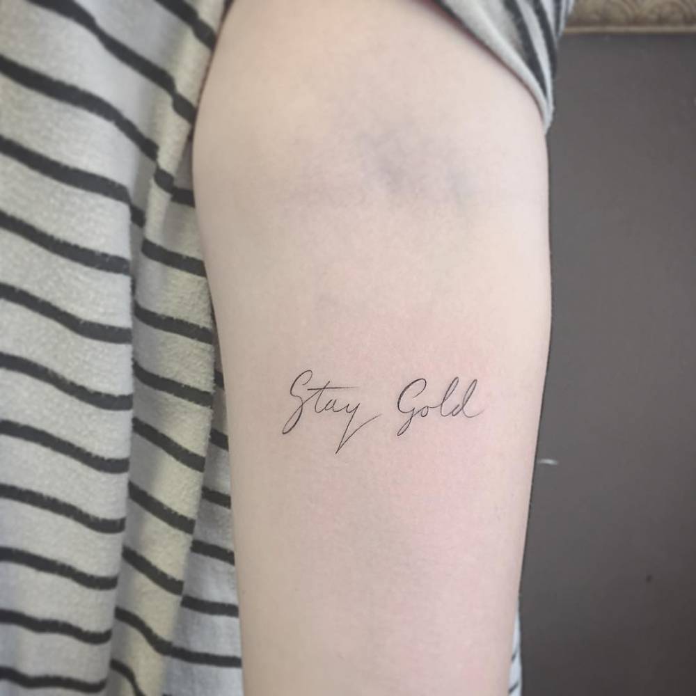 "Stay gold" tattoo on the left forearm.