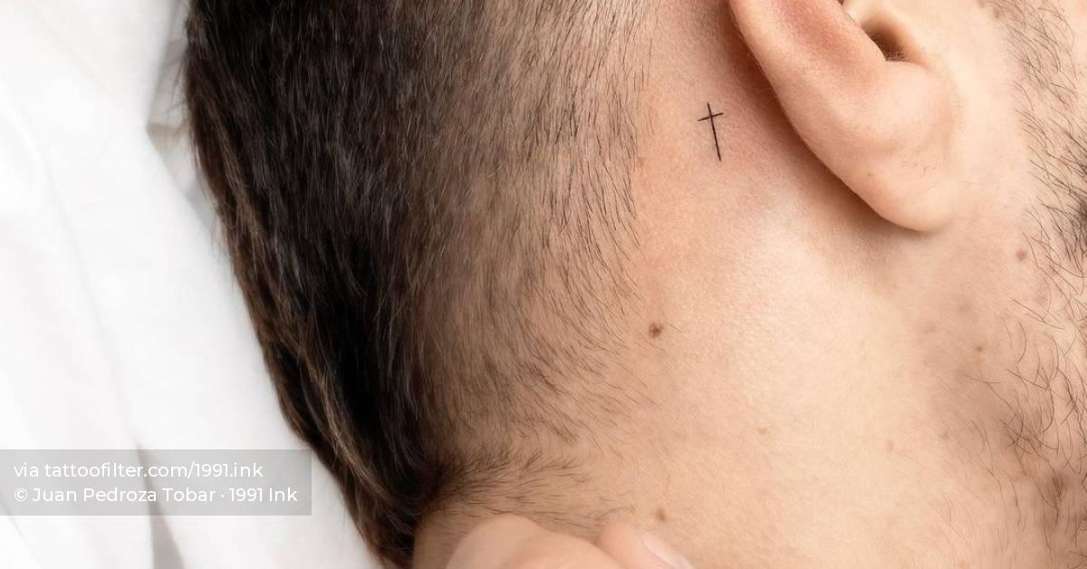 Minimalist cross tattoo behind the ear.