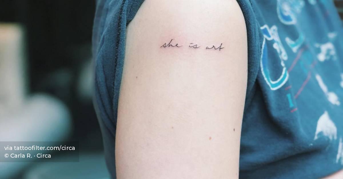 "She is art" lettering tattoo on the shoulder.
