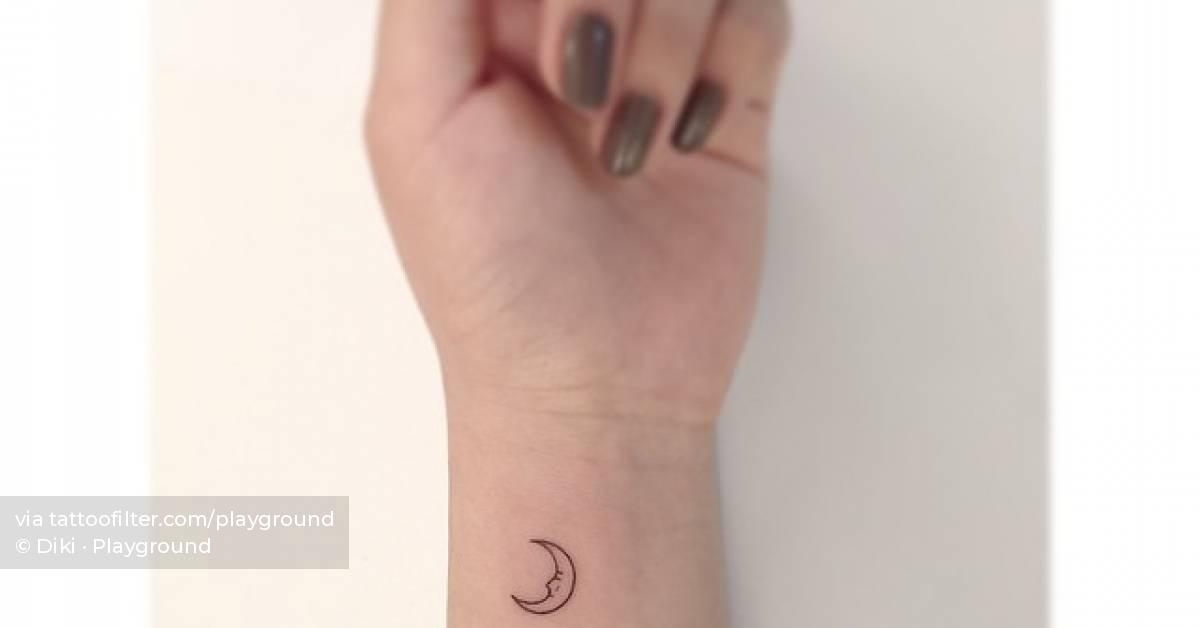 Fine line moon face tattoo located on the wrist.