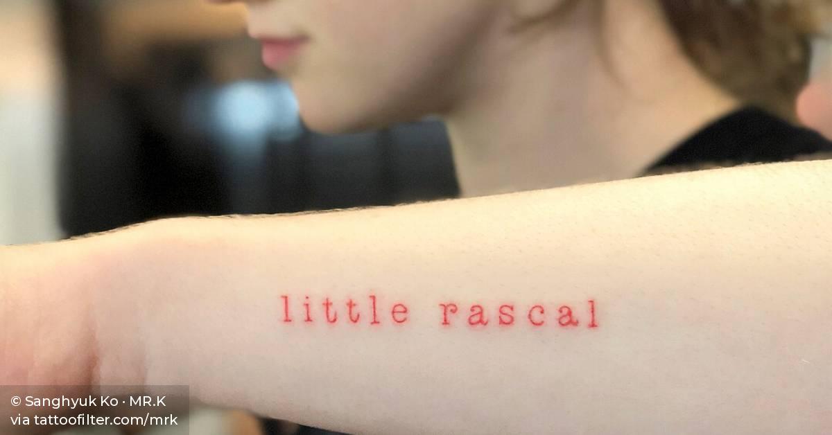 Red ink “little rascal” tattoo on the forearm.
