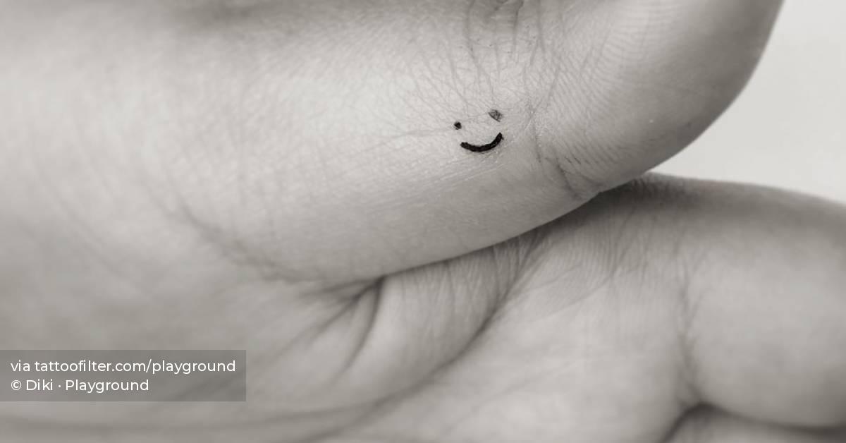 Minimalistic birthmark smiley tattooed on the finger.