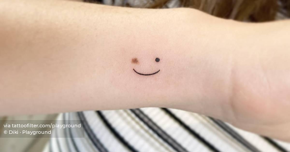 Minimalistic birthmark smiley tattooed on the wrist.