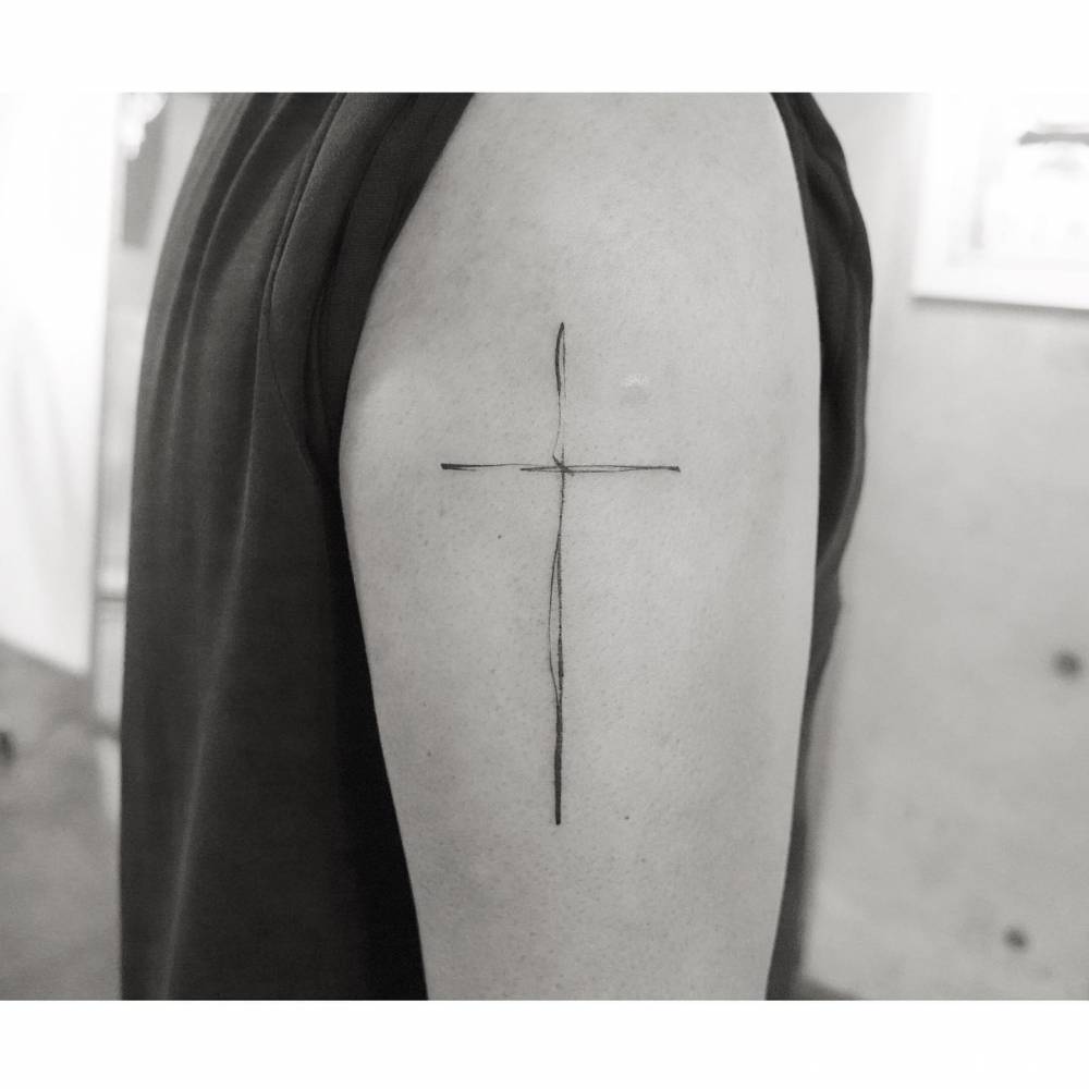 Fine Line Cross Tattoo Located On The Upper Arm 