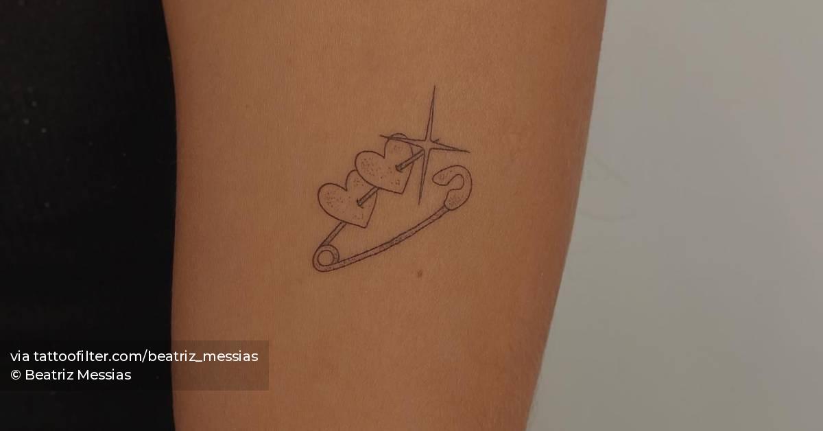 Safety pin and hearts tattoo located on the upper arm.