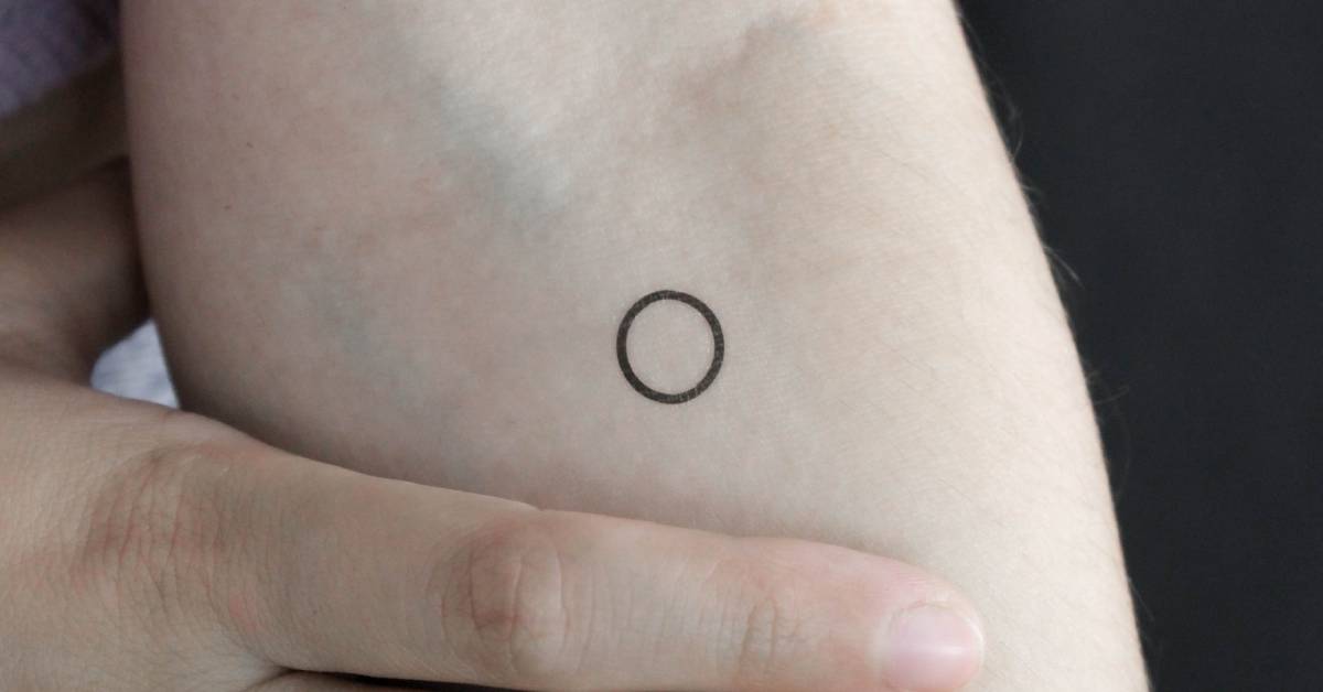 Tiny minimalistic circle temporary tattoo located on