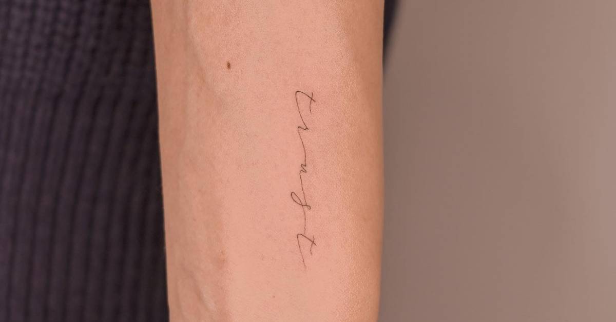 Tattoo of the word "trust" handwritten on the wrist.
