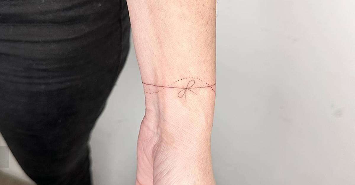 Fine line style ribbon wristband tattoo.