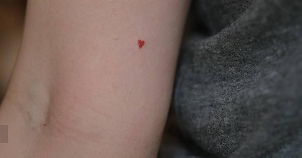 Tiny minimalistic red heart tattoo located on the inner