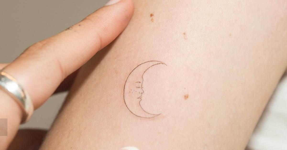 Fine line style crescent moon face tattoo located on
