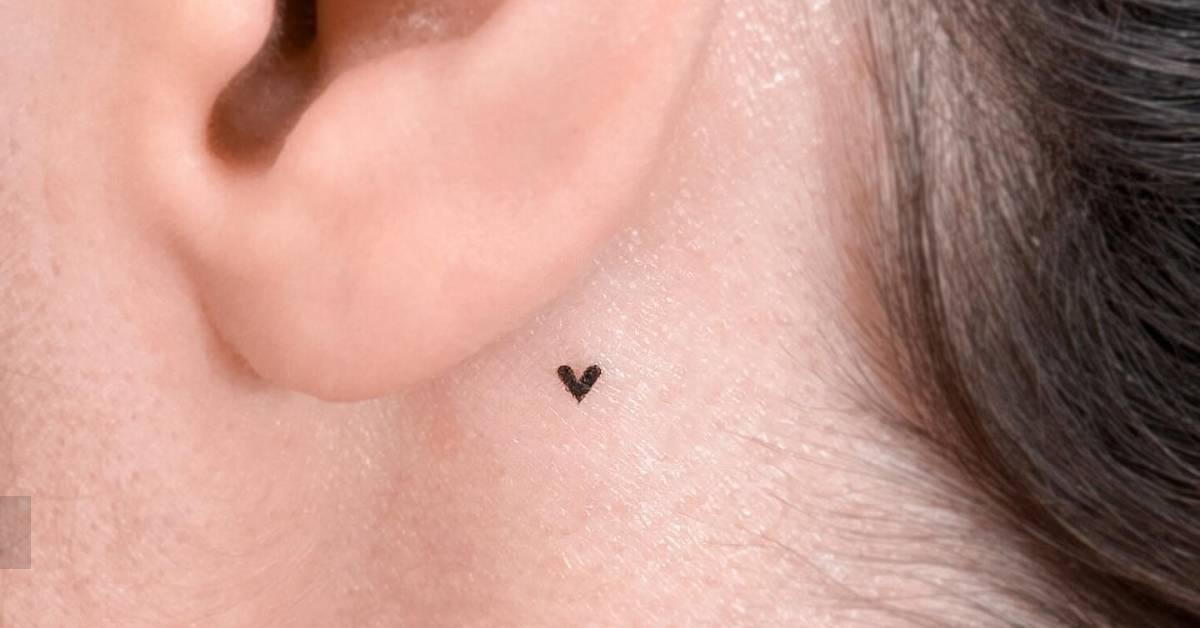 Tiny minimalistic heart tattoo located behind the ear.