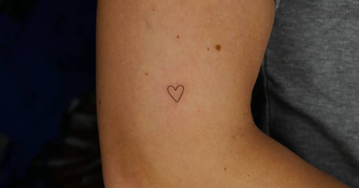 Tiny minimalistic heart tattoo located on the upper