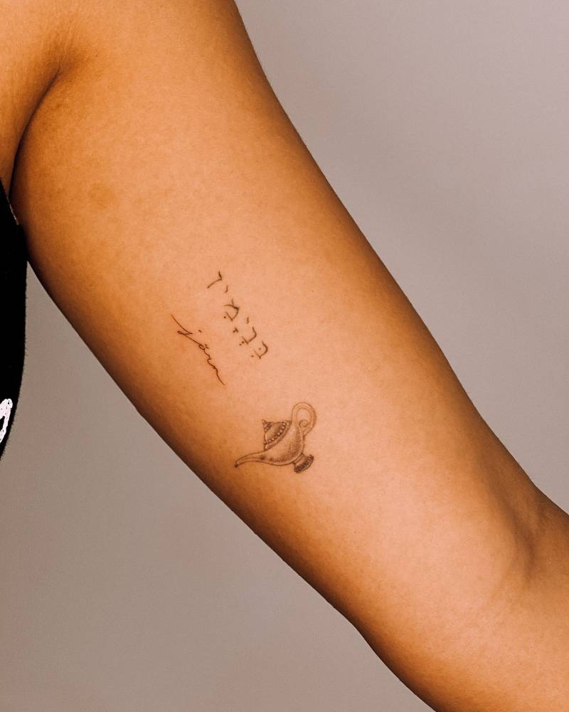 Genie lamp and lettering tattoo located on the inner arm.