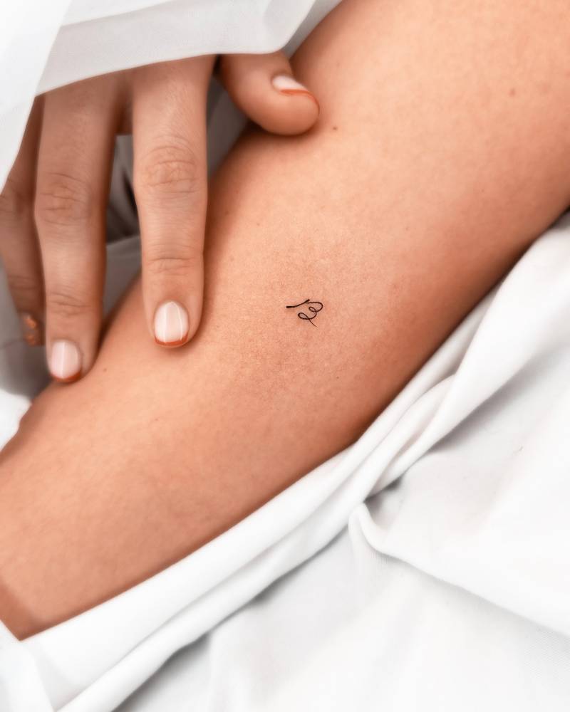 Tiny handwritten letter "B" tattoo located on the forearm.