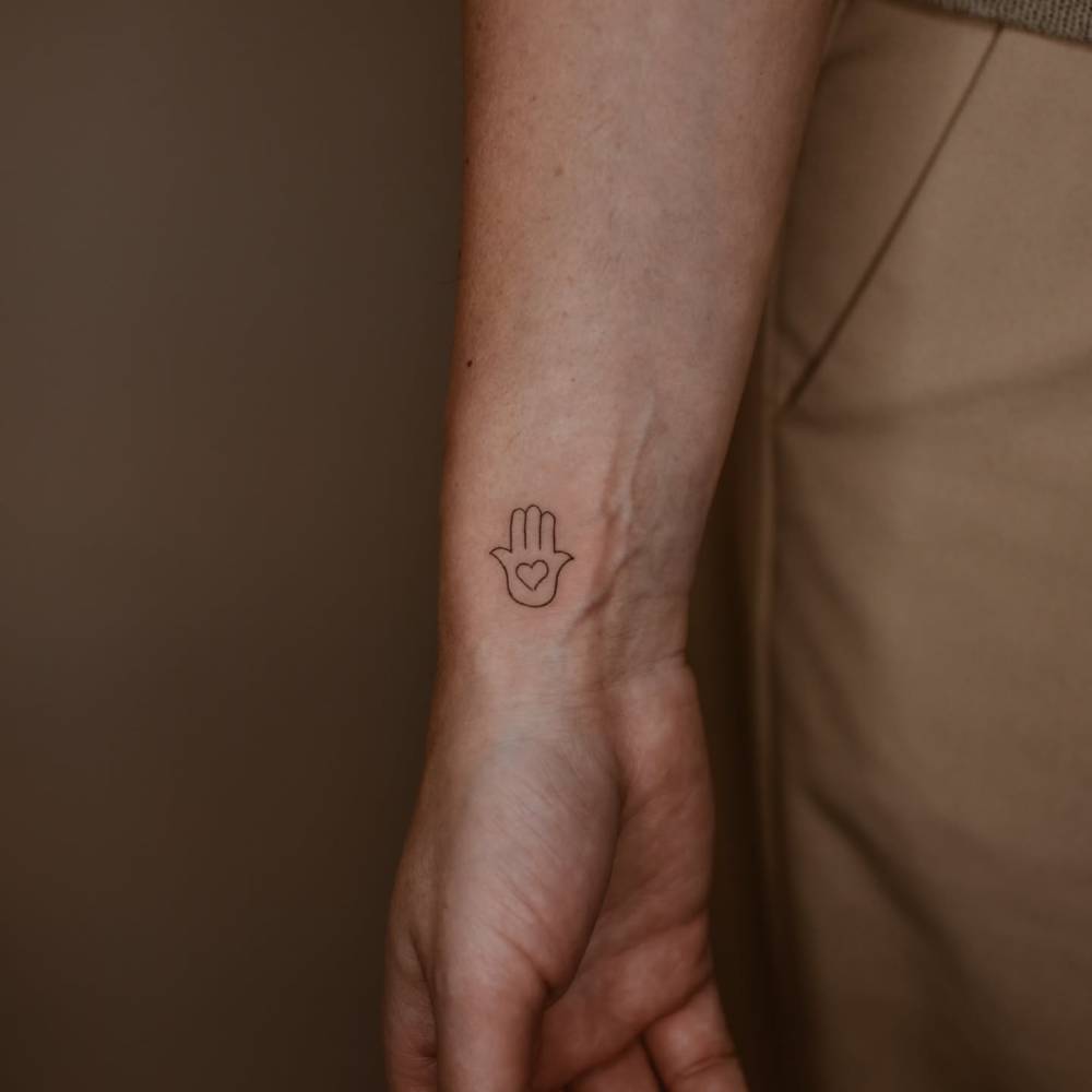 Fine line style little Hamsa tattoo located on the wrist.