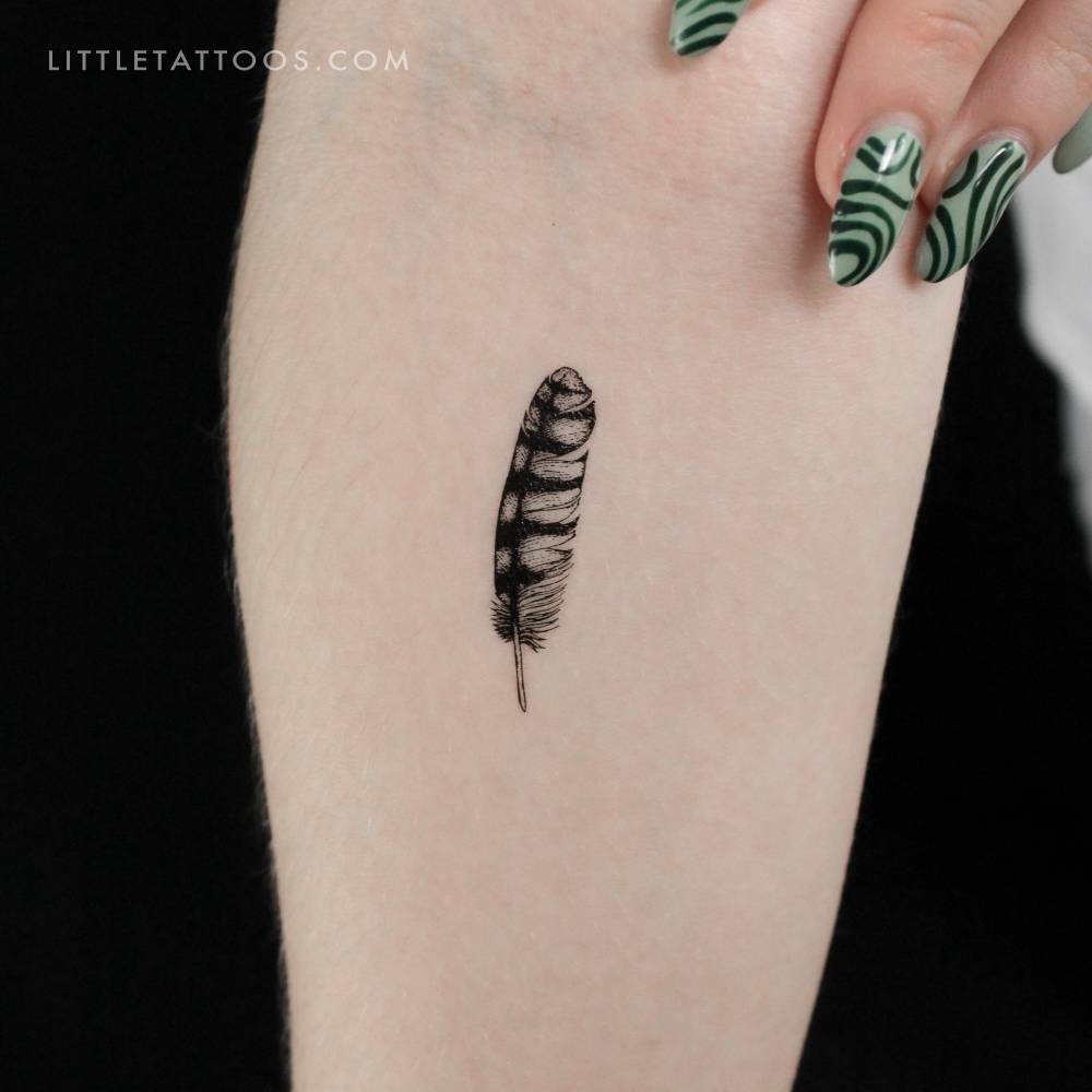 Illustrative style small feather temporary tattoo located on the inner forearm.