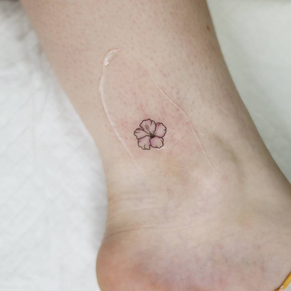 Minimalistic style hibiscus flower tattoo located on the ankle.