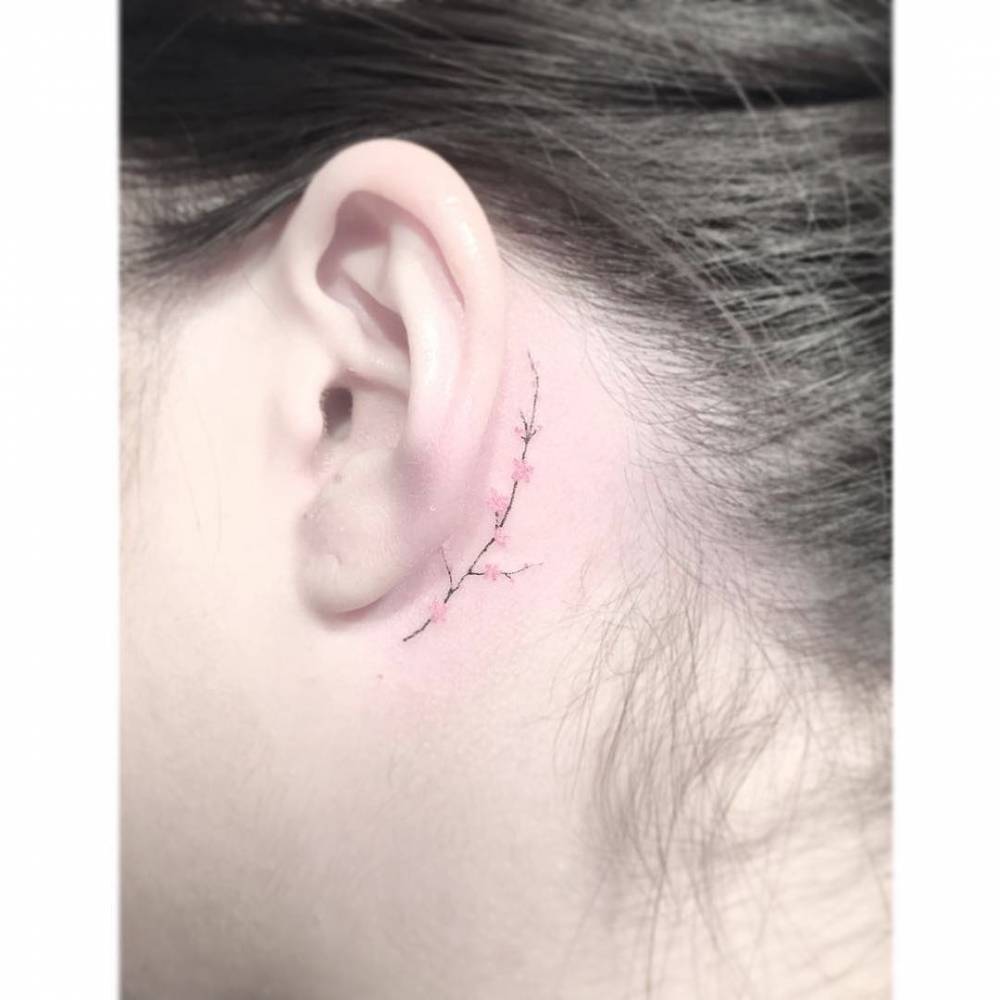 Tiny minimalistic cherry blossom tattoo located behind the ear.