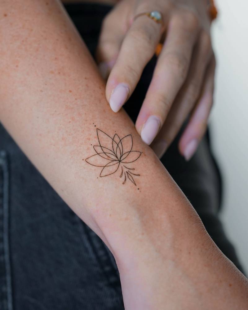Fine line style lotus flower tattoo located on the wrist.