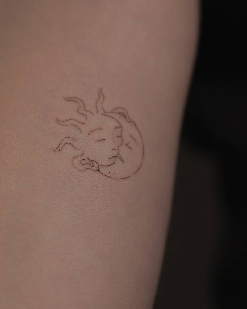 Fine line style kissing sun and moon tattoo located on the inner forearm.