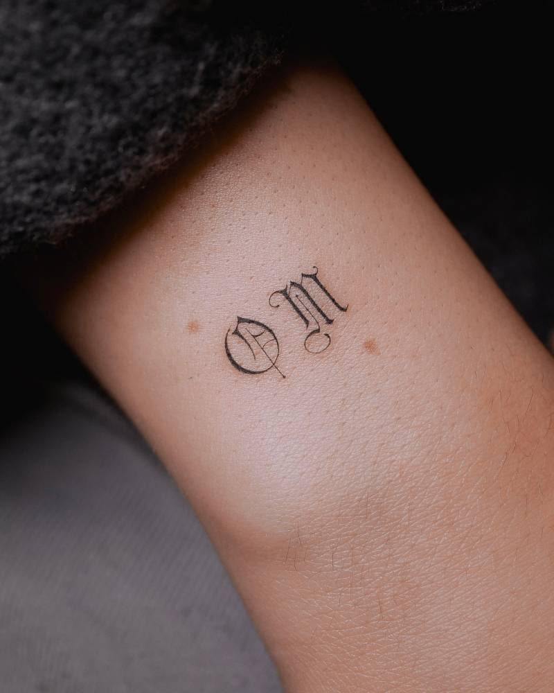 Gothic font "om" tattoo located on the wrist.