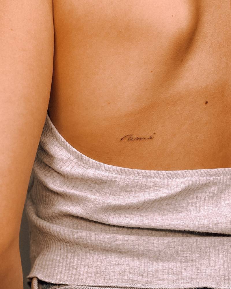 "Amé" handwritten lettering tattoo  located on the back.