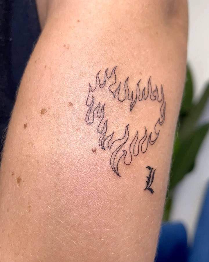 Flaming heart and letter "L" tattoo located on the forearm.
