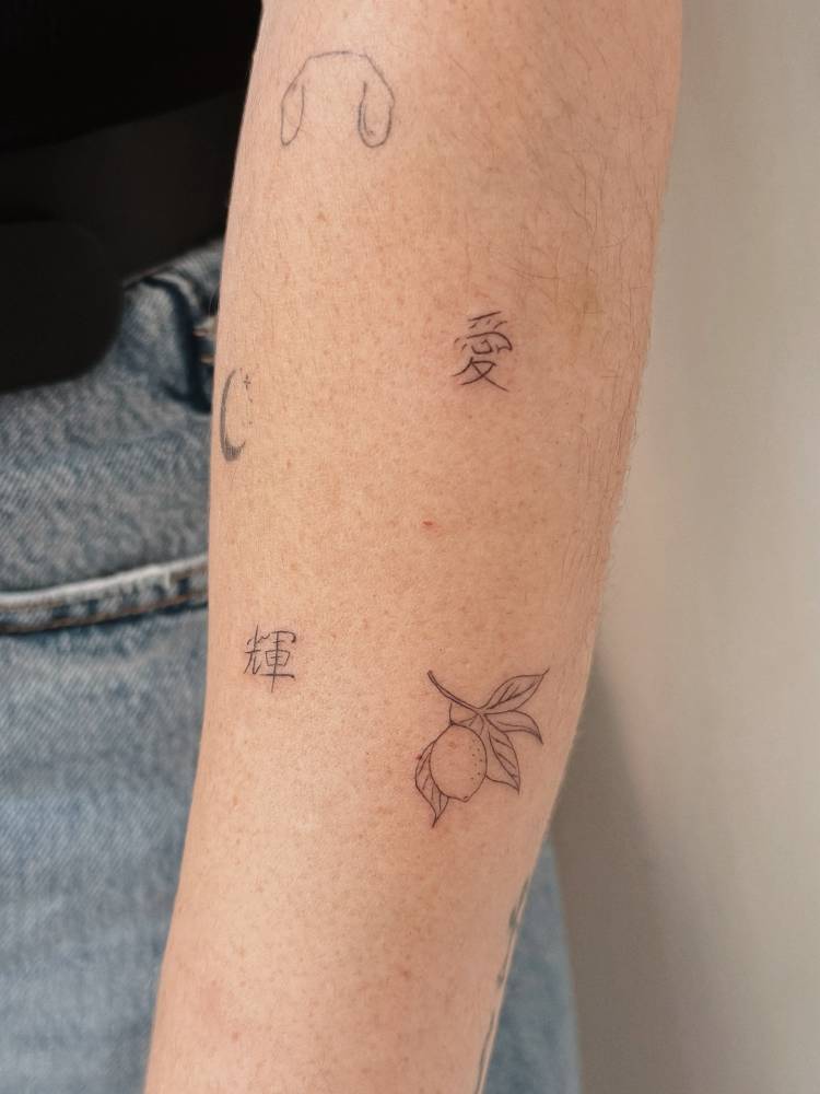 Lemon and Chinese characters tattooed on the forearm, fine line style.