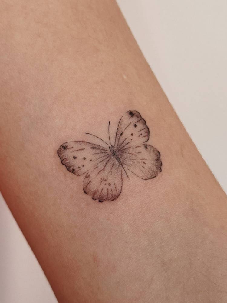 Watercolor style butterfly tattoo placed on the bicep.