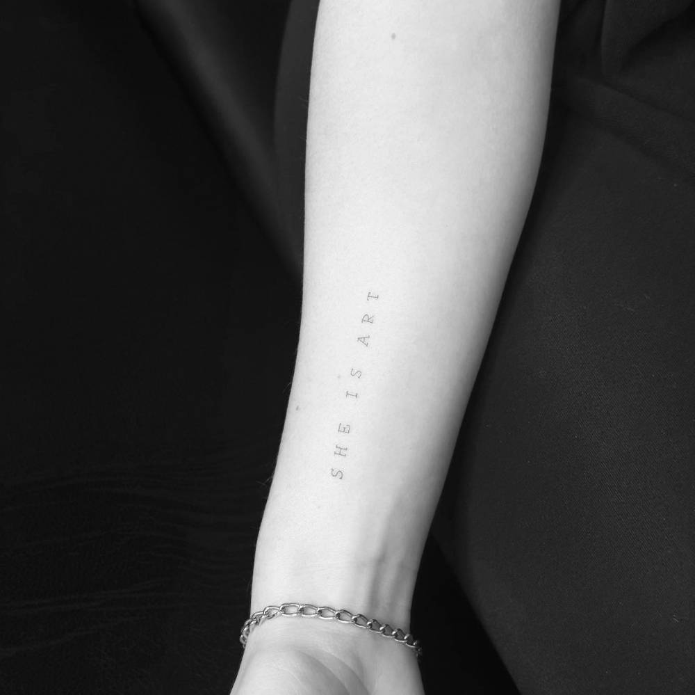 "She is art" lettering tattoo located on the wrist.