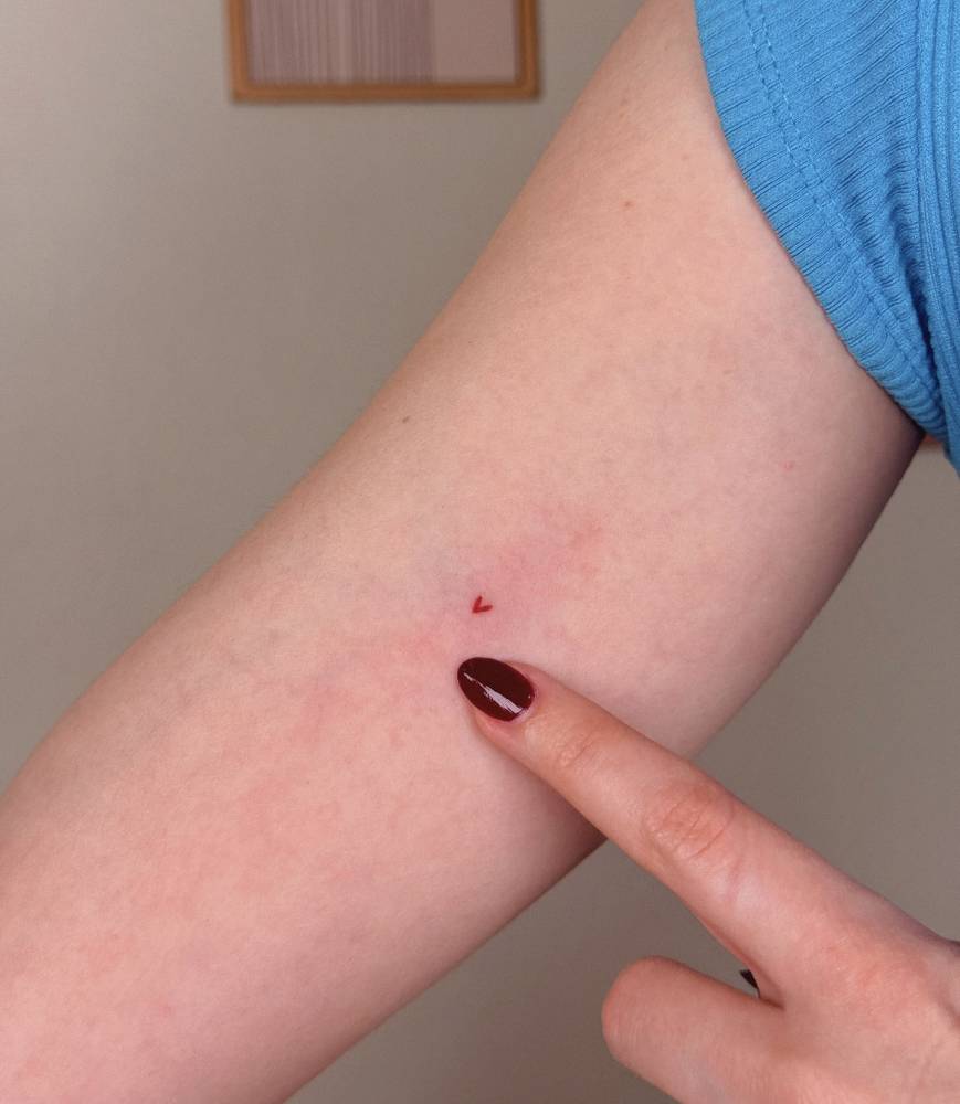 Tiny minimalistic red heart tattoo located on the inner arm.