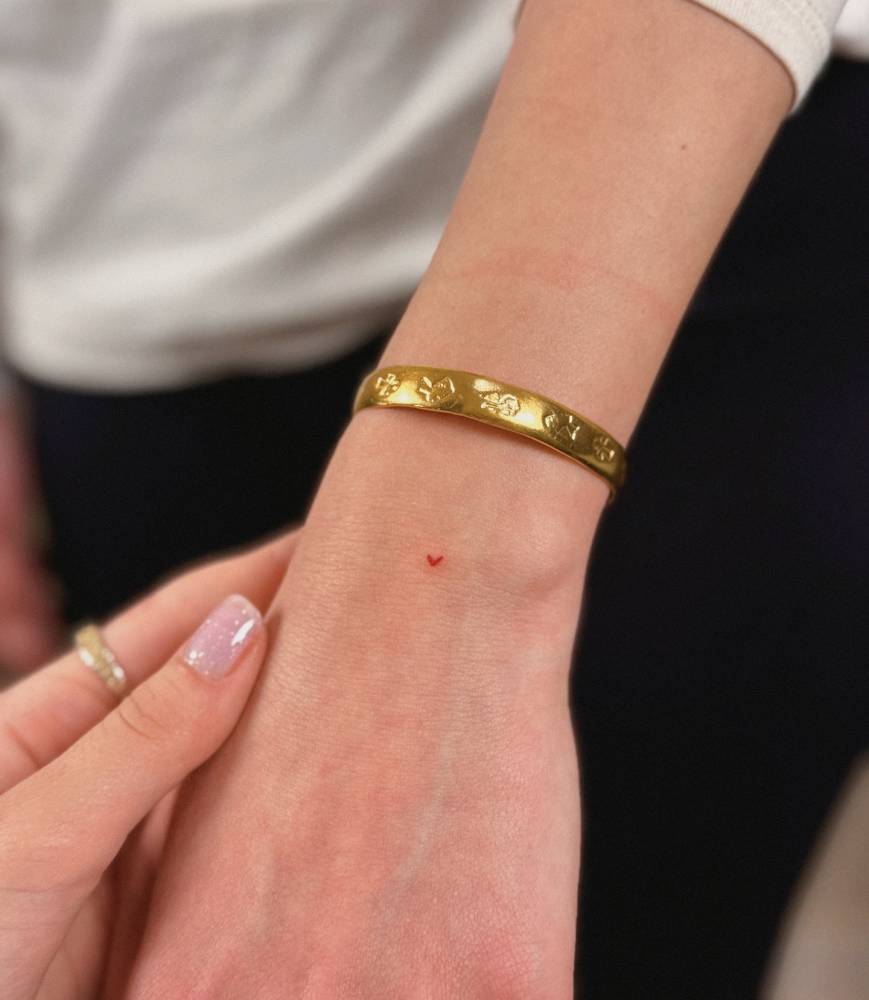 Micro tattoo of a red heart in minimalistic style placed on the wrist.