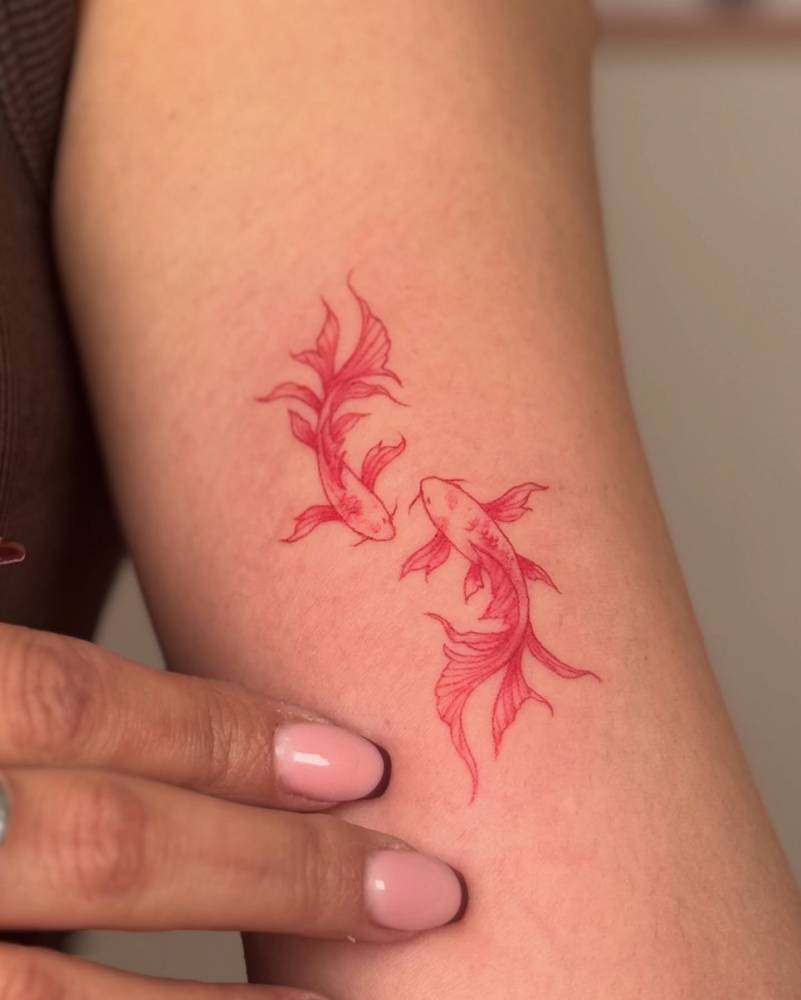 Two opposite fish tattoo in red ink located on the inner arm.