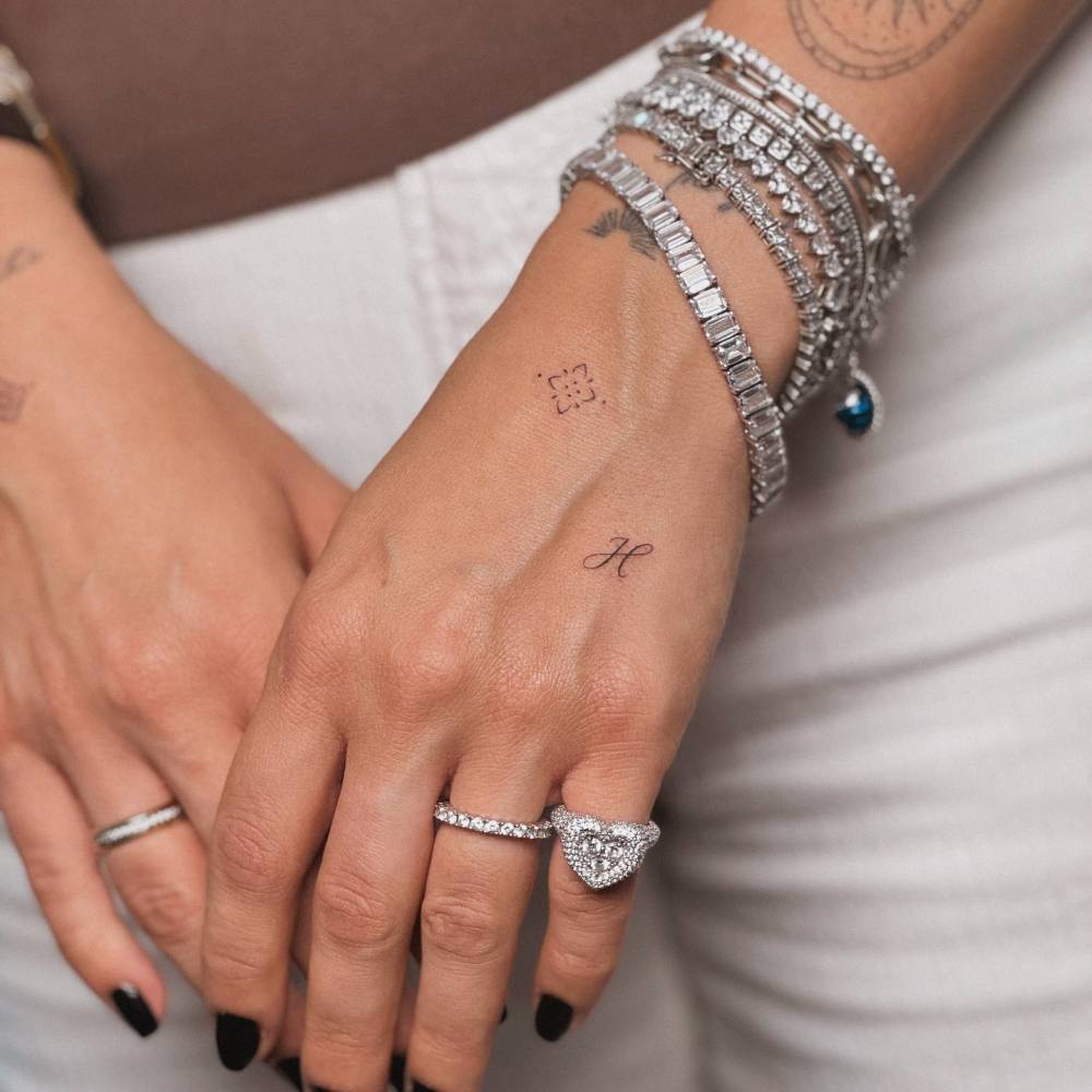 Ornament and letter "H" tattoo located on the hand.