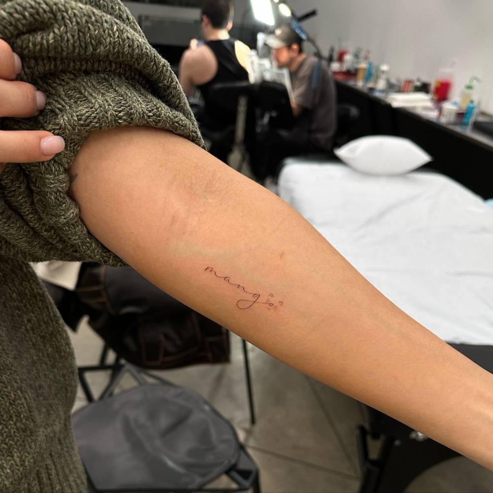 Name "Mango" with a cat face tattooed on the inner forearm.