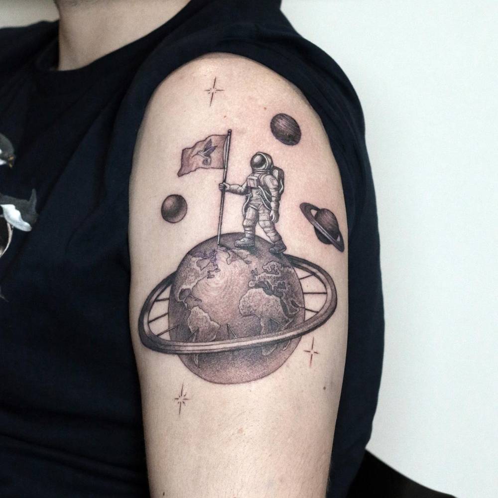 Illustrative style astronaut and planet Earth tattoo placed on the upper arm.