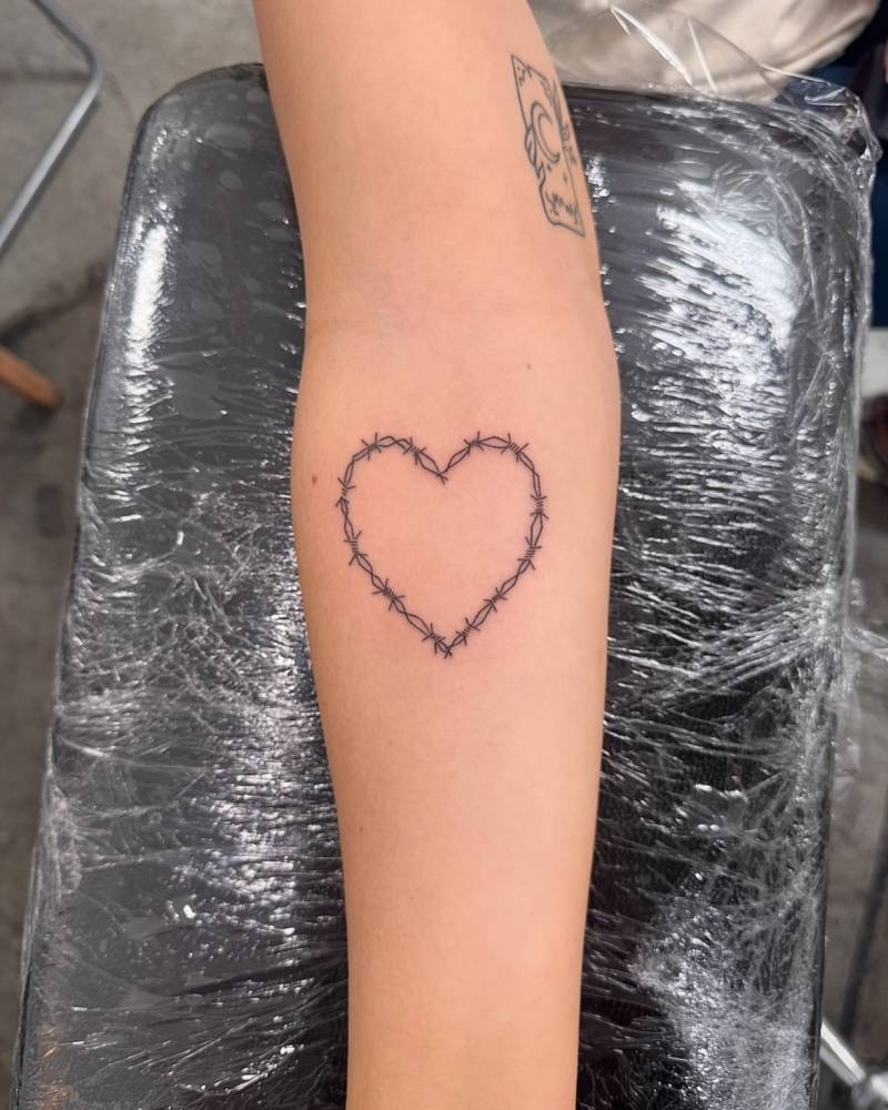 Fine line style barbed wire heart tattoo located on the inner forearm.