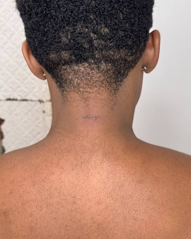 Tiny handwritten lettering tattoo placed on the back of the neck.
