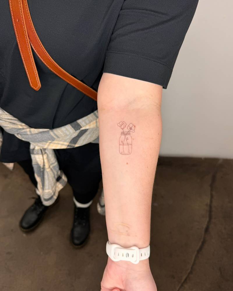 Fine line style flowers in a bottle tattoo located on the inner forearm.