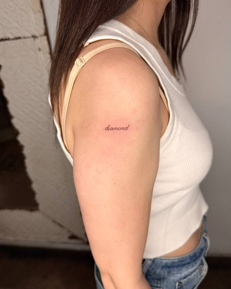 "Diamond" lettering tattoo in script font located on the upper arm.