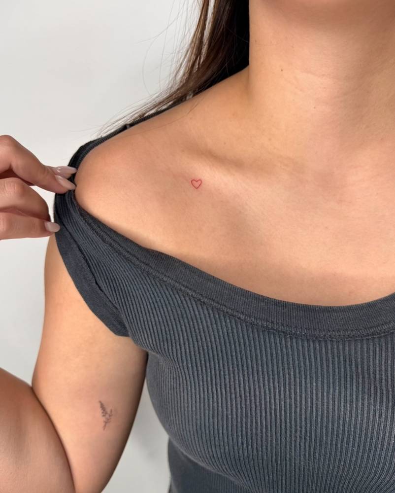 Tiny minimalistic red heart tattoo placed on the collarbone.