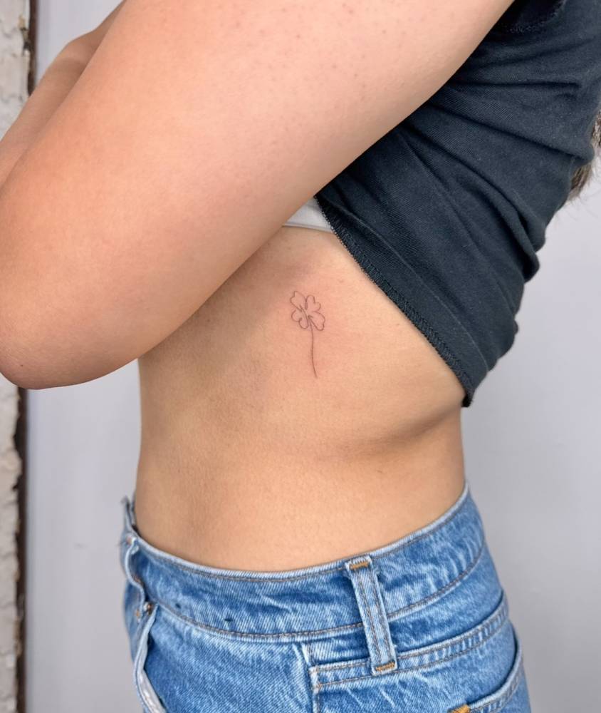 Four leaf clover tattoo in fine line style located on the rib.