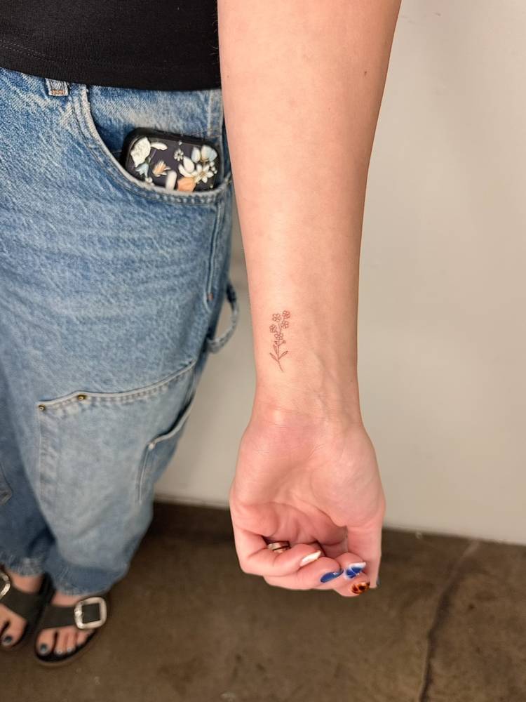 Little flowers tattoo in fine line style placed on the wrist.
