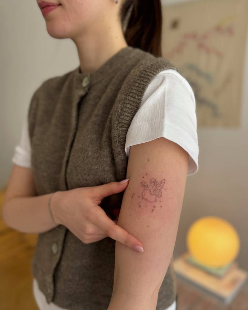 Little fine line style fairy tattoo placed on the upper arm.