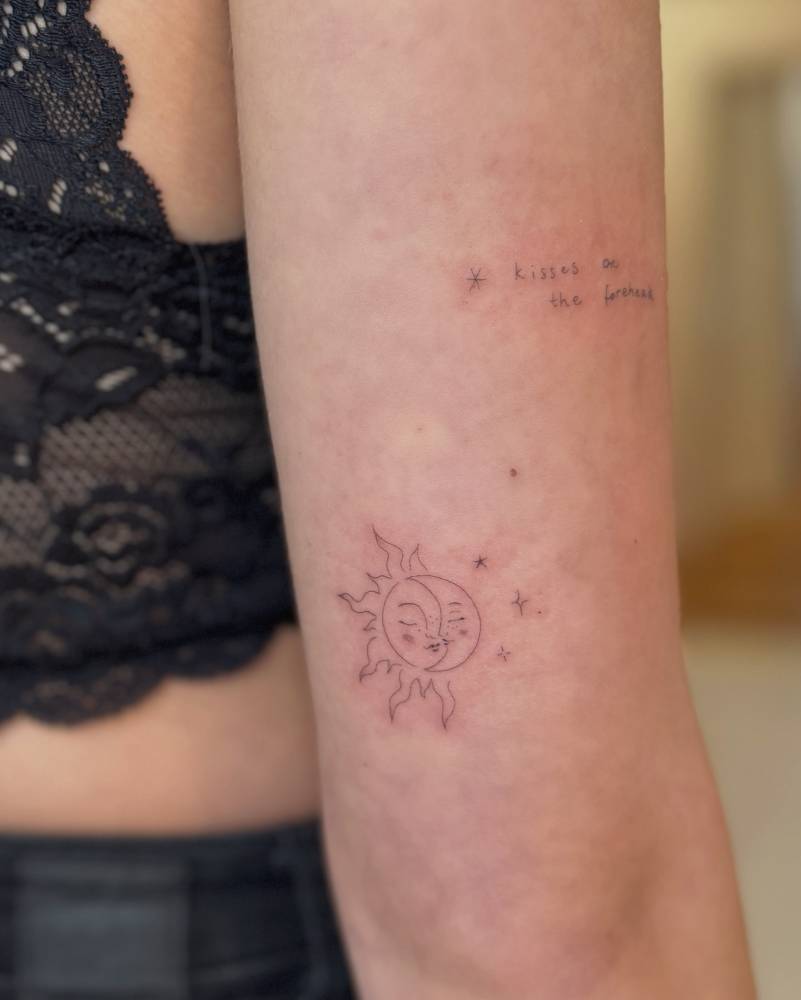Kissing sun and moon tattoo located on the tricep.