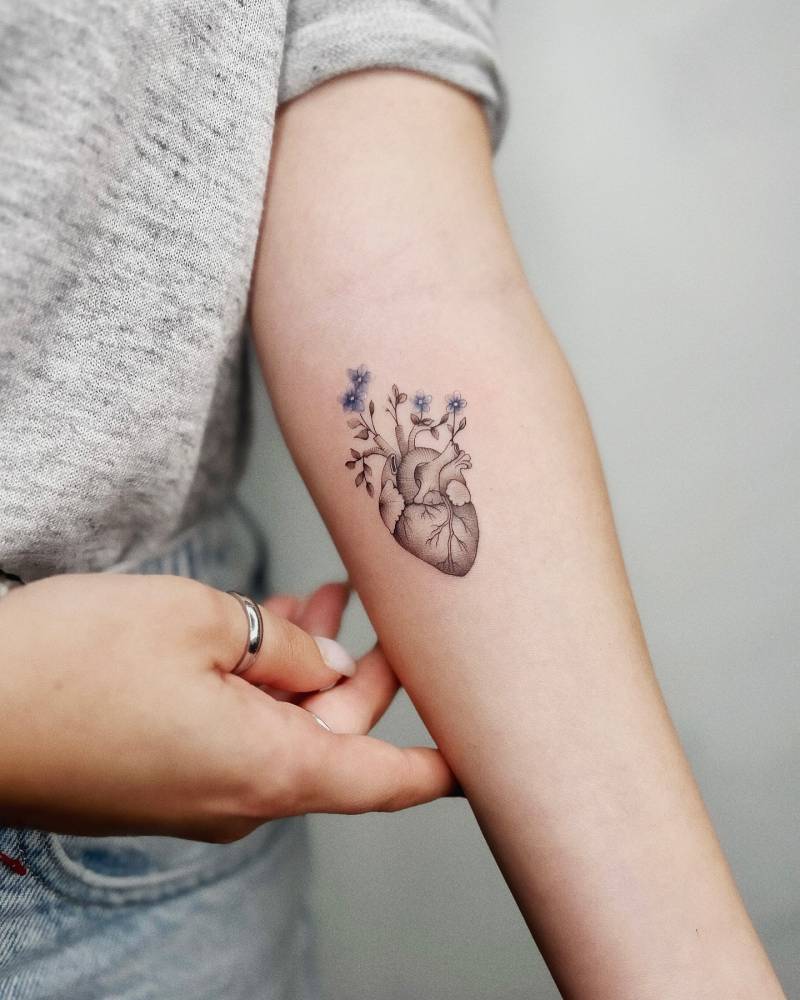 Illustrative style anatomical heart with flowers tattoo placed on the inner forearm.