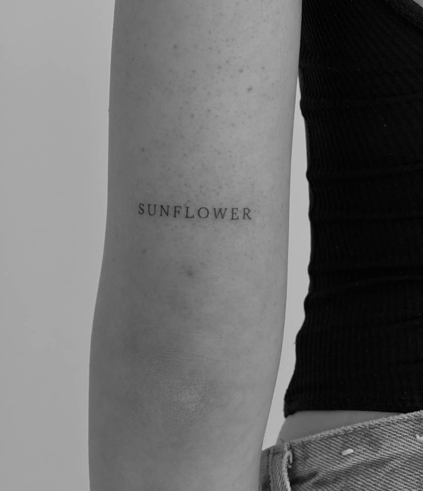 Serif font word "sunflower" tattooed on the tricep.