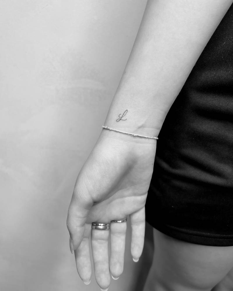Handwritten letter "L" tattoo located on the wrist.