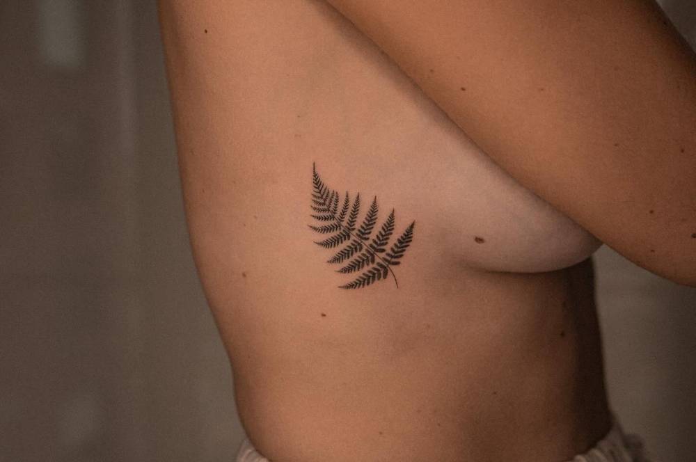 Micro-realistic style fern leaf tattoo located on the side boob.